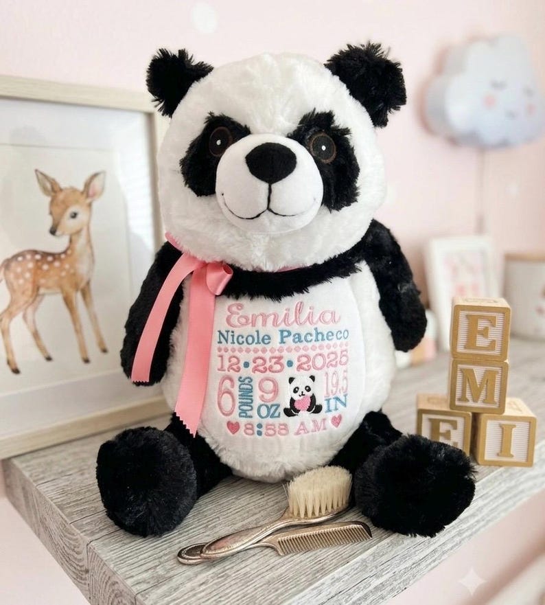 Może przedstawiać: Pluszowa zabawka panda z czarno-białym futrem i r&oacute;żową wstążką na szyi. Biały brzuch jest wyhaftowany imieniem Emilia Nicole Pacheco, datą 23-12-2025, wagą 6 funt&oacute;w 9 uncji, wzrostem 19,5 cala oraz godziną 8:58 w kolorze r&oacute;żowym i niebieskim.