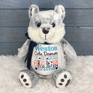 May include: A plush wolf stuffed animal with gray and white fur, a navy blue ribbon, and embroidered details. The wolf has a white belly with embroidered text: "Weston Cole Damon 05-20-2022 6 pounds 15 oz 19 in 10:45 PM".