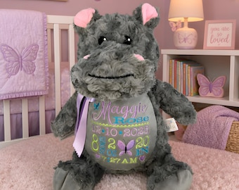 May include: A plush gray hippopotamus toy with pink inner ears and a light purple ribbon around its neck. The belly features embroidered text reading Maggie Rose, 12-10-2025, 8 pounds 2 ounces, 20 inches, and 7:27 AM, accented with butterfly designs.