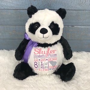May include: A black and white panda plush toy with a purple ribbon. The panda has a white heart-shaped patch on its chest with embroidered text: "Skyler Elizabeth Piccone 12.25.2021 8 pounds 1 oz 21 in Columbia SC 1:41 PM".