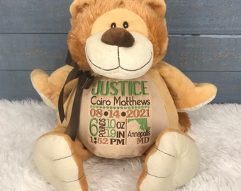 May include: A plush tan teddy bear with a dark brown ribbon around its neck. The bear features embroidered text including the name Justice, Cairo Matthews, the date 08-14-2021, birth stats of 6 pounds 10 ounces, 19 inches, 1:52 PM, and Annapolis MD.