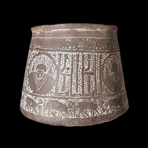 May include: A brown ceramic pot with a wide base and a narrow opening. The pot is decorated with incised designs of figures and animals.
