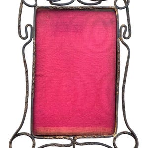 May include: A black metal picture frame with a decorative scrolled design. The frame has a red velvet backing.