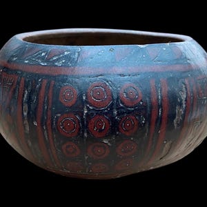 May include: A round, black ceramic bowl with red and white geometric designs. The bowl has a slightly rounded bottom and a wide opening.