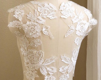 May include: White lace applique with floral designs and sequins. The applique is on a white dress form.