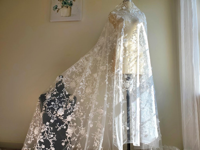 May include: White lace fabric with a floral pattern. The lace is delicate and has a soft, flowing texture.