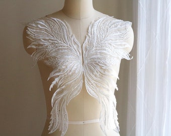 May include: White lace applique with a feather design. The applique is on a white mannequin and has a delicate, intricate pattern.