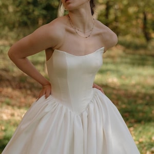 May include: A strapless white satin wedding dress with a fitted bodice and a full skirt.