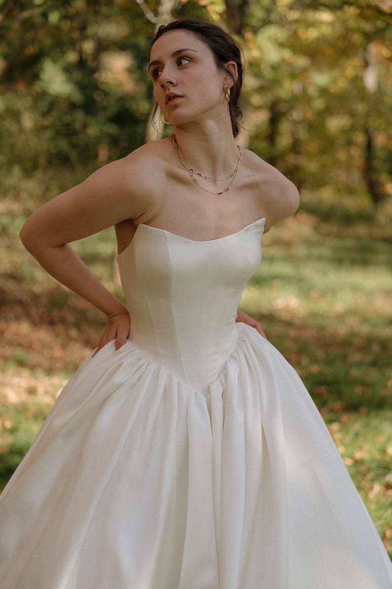 May include: A strapless white satin wedding dress with a fitted bodice and a full skirt.