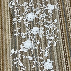 May include: White lace trim with floral designs. The lace features delicate flowers and leaves, perfect for adding a touch of elegance to any project.
