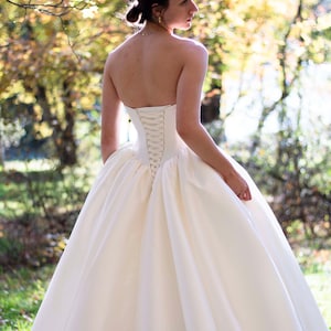 May include: A white strapless wedding dress with a lace-up back detail. The dress has a full skirt and is made of a smooth, satin fabric.