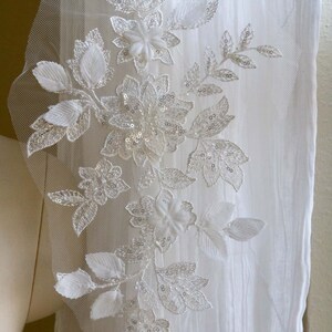 May include: White floral lace applique with sequins and beads. The lace is delicate and intricate, with a floral design. The applique is perfect for adding a touch of elegance to any project.