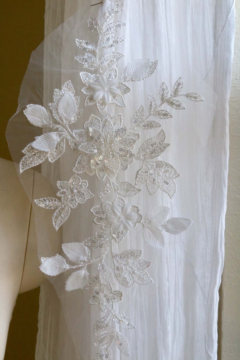 May include: White floral lace applique with sequins and beads. The lace is delicate and intricate, with a floral design. The applique is perfect for adding a touch of elegance to any project.