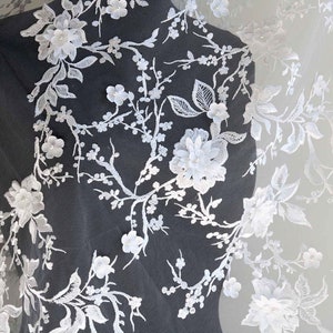 May include: White floral lace fabric with delicate 3D flowers and intricate designs. The lace is soft and sheer, perfect for adding a touch of elegance to any project.