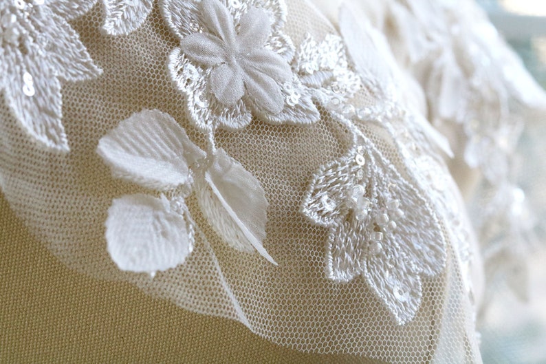 May include: White lace fabric with floral embroidery and sequins. The fabric has a delicate, feminine look and would be perfect for a wedding dress or other special occasion garment.