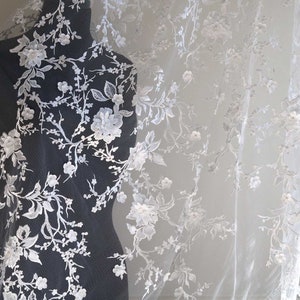 May include: White floral lace fabric with delicate embroidery and 3D flowers. The lace is sheer and has a soft, romantic feel.