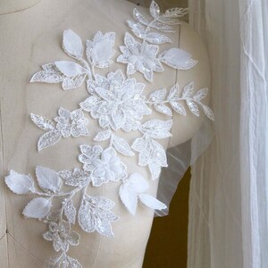 May include: White floral lace applique with sequins and beads. The applique is on a white mesh fabric and has a delicate design with leaves and flowers.