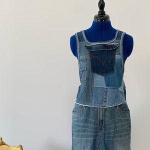 May include: A patchwork denim maxi dress displayed on a blue mannequin. The dress has a bib top, pockets, and a long skirt with a front split. Various denim shades are patched together. A Levi's label is visible.