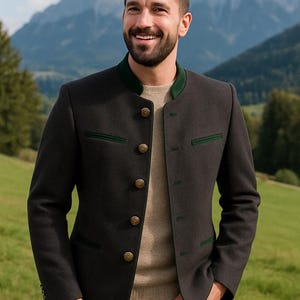 May include: A dark gray jacket with green trim and gold buttons. The jacket has a stand-up collar and is worn over a tan sweater and blue jeans. The background features a mountain range and green field.