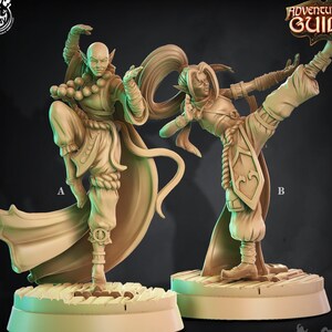 Könnte beinhalten: Zwei unbemalte Miniaturfiguren von Elfenmönchen in Kampfstellung. Der Mönch links trägt eine Robe und der Mönch rechts trägt eine Hose und ein Hemd. Beide Figuren stehen auf runden Sockeln. Der Text "Elvish Monks 457" ist unter den Figuren gedruckt.