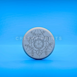 May include: A circular, gray, decorative object with a design of a circle with five smaller circles around it. The object has text around the outer edge, which reads "Ash nazg durbatulûk, ash nazg gimbatul, ash nazg thrakatulûk, agh burzum-ishi krimpatul."