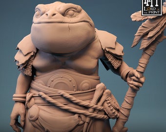 Op de afbeelding: Een 3D-geprint miniatuur van een kikkerachtig wezen dat een harnas draagt en een staf vasthoudt. Het wezen heeft een groot hoofd en een brede mond. De staf is versierd met veren. Het miniatuur is geschilderd in een lichtbruine kleur. De tekst "THE SHELLBACK RITUAL" is onder het miniatuur gedrukt.