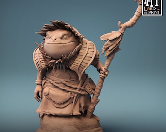 Op de afbeelding: Een 3D-geprint miniatuur van een kikkerachtig wezen dat een verenhoed draagt en een staf vasthoudt. Het miniatuur is in lichtbruin geverfd en staat op een voetstuk. De tekst "The Shellback Ritual" is onder het miniatuur gedrukt.
