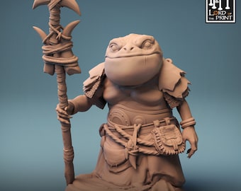 Op de afbeelding: Een miniatuurfiguur van een kikkerachtig wezen dat een lendendoek draagt en een staf vasthoudt. Het figuur is gemaakt van lichtbruin materiaal en heeft een gedetailleerd ontwerp. Het figuur is getiteld "The Shellback Ritual".