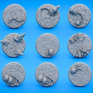 May include: Nine grey, circular miniature bases with textured, cracked earth designs. Some bases feature chains, rocks, skulls, and foliage, ideal for tabletop gaming or model building.