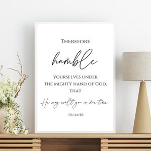 Puede incluir: Una impresión enmarcada en blanco con una cita inspiradora en blanco y negro que dice "Therefore humble yourselves under the mighty hand of God, that He may exalt you in due time. 1 Peter 5:6". La impresión está sobre un estante de madera con un sillón blanco y una lámpara en el fondo.