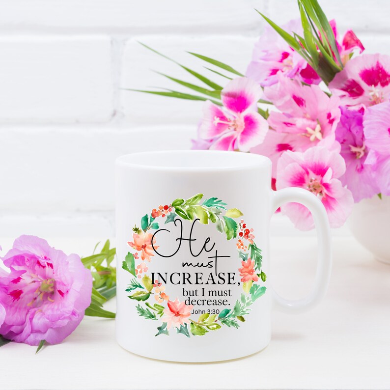 Pu&ograve; includere: Tazza in ceramica bianca con un design a corona di fiori e il testo "He must increase, but I must decrease. John 3:30".