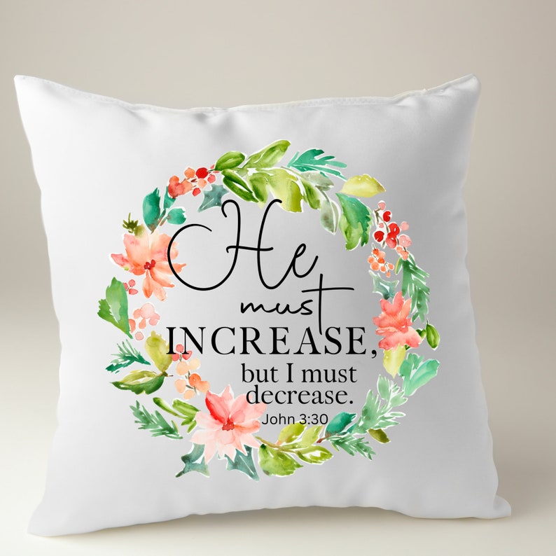 Pu&ograve; includere: Un cuscino bianco con un design a corona di fiori. La corona &egrave; fatta di foglie verdi, fiori rosa e rossi e bacche. Il testo sul cuscino recita "Egli deve crescere, ma io devo diminuire. Giovanni 3:30".