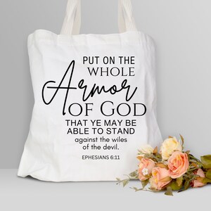 May include: White canvas tote bag with black text that reads "Put on the whole Armor of God. That ye may be able to stand against the wiles of the devil. Ephesians 6:11"