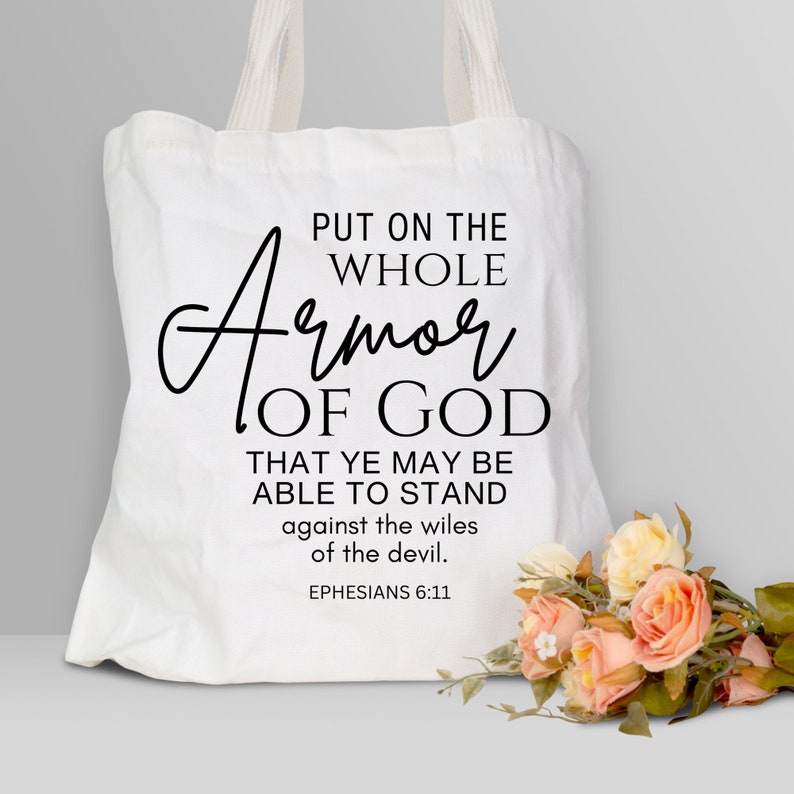 May include: White canvas tote bag with black text that reads "Put on the whole Armor of God. That ye may be able to stand against the wiles of the devil. Ephesians 6:11"
