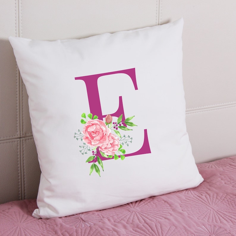 K&ouml;nnte beinhalten: Wei&szlig;er Kissenbezug mit einem rosafarbenen Blumendesign und dem Buchstaben "E" in Magenta.