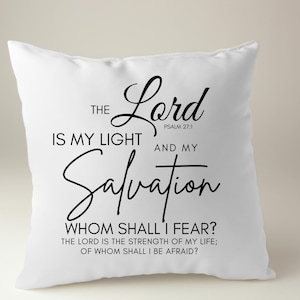 Op de afbeelding: Wit kussen met zwarte tekst die luidt: "De Heer is mijn licht en mijn redding. Psalm 27:1. Wie zal ik vrezen? De Heer is de kracht van mijn leven; voor wie zal ik beven?"