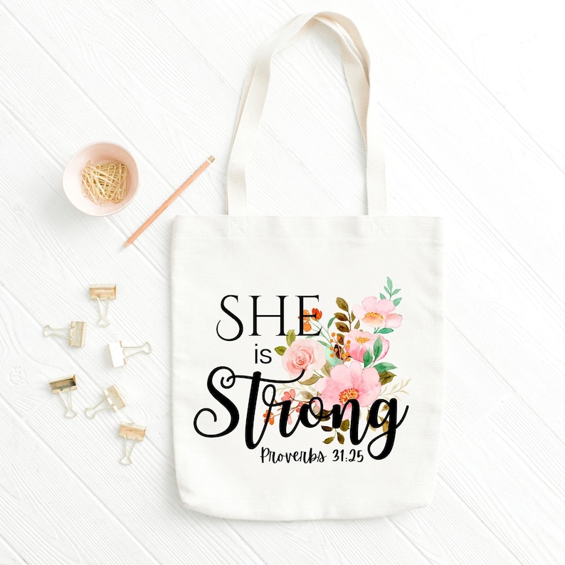 May include: White canvas tote bag with a floral design and the text "SHE is Strong Proverbs 31:25"
