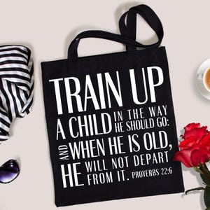 May include: Black tote bag with white text that reads "TRAIN UP A CHILD IN THE WAY HE SHOULD GO: AND WHEN HE IS OLD, HE WILL NOT DEPART FROM IT. PROVERBS 22:6". The bag has two black handles.