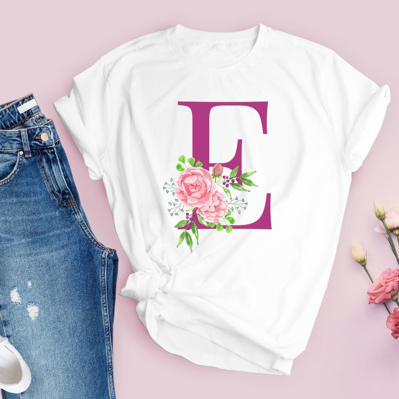 K&ouml;nnte beinhalten: Wei&szlig;es T-Shirt mit einem rosafarbenen Blumendesign und dem Buchstaben "E" in Magenta.