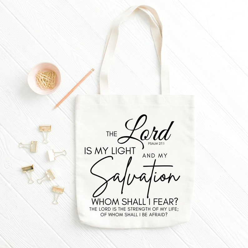 Op de afbeelding: Witte canvas tote bag met zwarte tekst die luidt: "The Lord is my light and my Salvation. Psalm 27:1. Whom shall I fear? The Lord is the strength of my life; of whom shall I be afraid?"