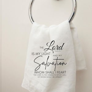 Op de afbeelding: Witte handdoek met zwarte tekst die luidt: "De Heer is mijn licht en mijn redding, Psalm 27:1. Wie zal ik vrezen? De Heer is de kracht van mijn leven; voor wie zal ik beven?"