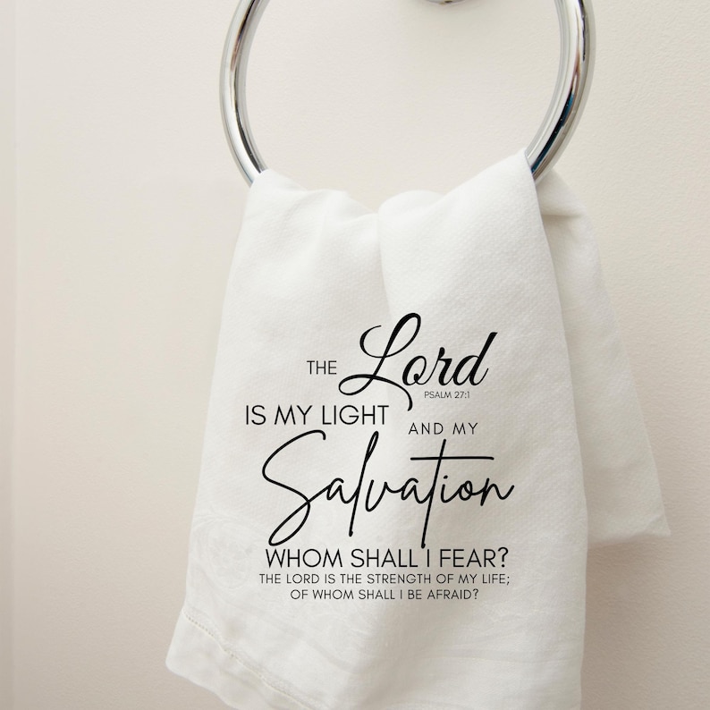 Op de afbeelding: Witte handdoek met zwarte tekst die luidt: "De Heer is mijn licht en mijn redding, Psalm 27:1. Wie zal ik vrezen? De Heer is de kracht van mijn leven; voor wie zal ik beven?"