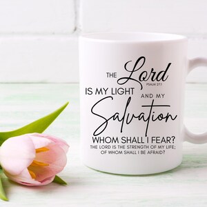 Op de afbeelding: Een witte keramische mok met zwarte tekst die "THE Lord IS MY LIGHT AND MY Salvation WHOM SHALL I FEAR? THE LORD IS THE STRENGTH OF MY LIFE; OF WHOM SHALL I BE AFRAID?" en "PSALM 27:1" zegt.