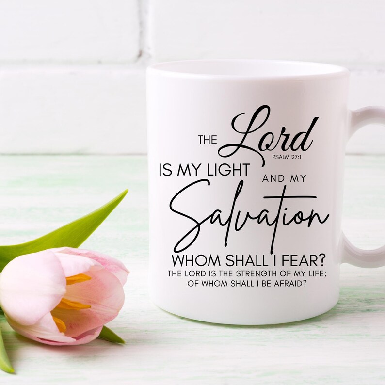 Op de afbeelding: Een witte keramische mok met zwarte tekst die "THE Lord IS MY LIGHT AND MY Salvation WHOM SHALL I FEAR? THE LORD IS THE STRENGTH OF MY LIFE; OF WHOM SHALL I BE AFRAID?" en "PSALM 27:1" zegt.