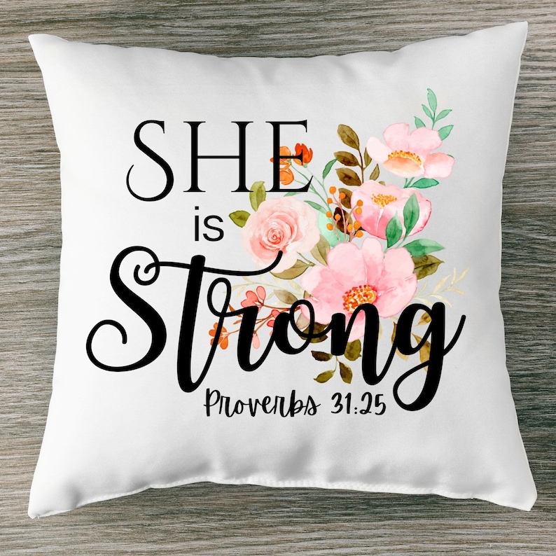 May include: White throw pillow with a floral design and the text "SHE is Strong Proverbs 31:25".
