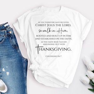 May include: White t-shirt with a black print of a Christian quote about Thanksgiving. The quote reads "As you therefore have received Christ Jesus the Lord, so walk in Him, rooted and built up in Him and established in the faith, as you have been taught, abounding in it with Thanksgiving." The quote is followed by "Colossians 2:6-7".
