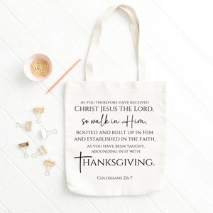 May include: A white canvas tote bag with black text that reads "AS YOU THEREFORE HAVE RECEIVED CHRIST JESUS THE LORD, SO WALK IN HIM, ROOTED AND BUILT UP IN HIM AND ESTABLISHED IN THE FAITH, AS YOU HAVE BEEN TAUGHT, ABOUNDING IN IT WITH THANKSGIVING. COLOSSIANS 2:6-7"