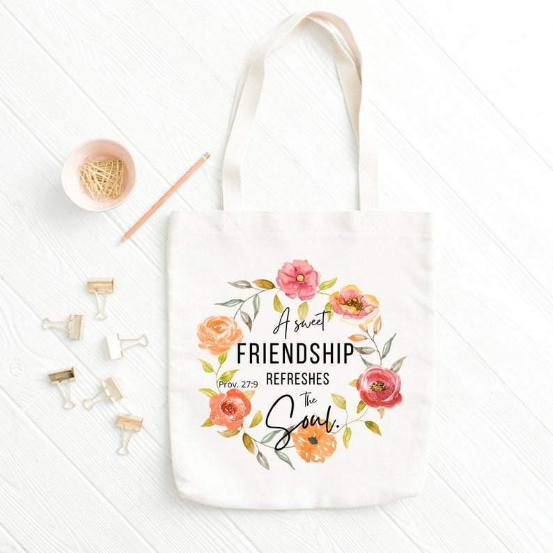 May include: A white canvas tote bag with a floral wreath design and the text "A sweet friendship refreshes the soul."  Prov. 27:9