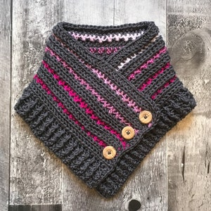 May include: A handmade, charcoal grey crochet cowl with pink and white stripes and three wooden buttons. The cowl is a cosy neck warmer, ideal for cooler weather. The design features a textured stitch pattern.