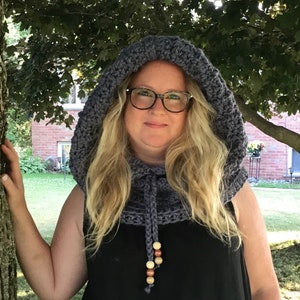 Pode incluir: Um capuz de crochê cinza feito à mão, com cordão e contas de madeira. O capuz foi projetado para ser usado ao redor do pescoço e sobre a cabeça. O capuz é feito de um fio grosso e texturizado.